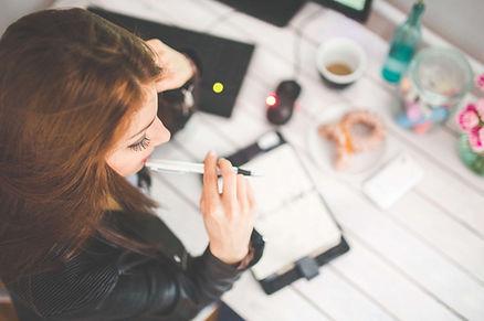 woman in black chewing on back of pen at desk